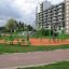 Des enfants jouent sur l'ensemble de terrain de jeu Single Swing avec des équipements verts et orange dans un parc urbain