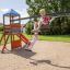 Deux enfants jouent sur un Double Swing with Tower playhouse with slide par une journée ensoleillée.