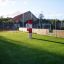 Ball catcher sur un terrain de jeu vert avec une clôture et un bâtiment en arrière-plan.