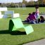 Chaise longue verte sur une pelouse de terrain de jeu avec des enfants qui jouent en arrière-plan