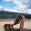 Sofa Wave, banc extérieur moderne en bois sur une surface sablonneuse dans un environnement urbain.