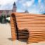 Banc en bois Sofa Wave sur une plage de sable avec un bâtiment en arrière-plan.