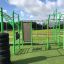 Équipement de fitness extérieur New Age Fit placé sur une zone herbeuse verte sous un ciel partiellement nuageux.