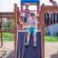 Trois enfants jouent sur un château Space Station avec un toboggan dans une aire de jeux.