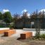 Terrain de sport extérieur avec clôtures vertes, bancs en bois et panier de basket, Multiarena.