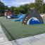 Dolphin Slide sur une aire de jeux avec revêtement en caoutchouc vert et des arbres en arrière-plan