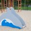 Toboggan de aire de jeux Dolphin Slide en forme de dauphin sur une aire de jeux sablonneuse.