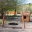 Ensemble de balançoires de terrain de jeu en bois BNS Single Swing Robinia 2 Posts à côté d'une petite maisonnette en bois.