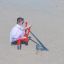 Enfant jouant sur un équipement de jeu rouge Excavator en train de creuser dans le sable.