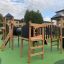 Aire de jeux Explorer castle with slide en bois et panneaux noirs sur surface verte.