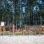 Course structure d’escalade et d’équilibre en bois pour aire de jeux dans une zone sablonneuse avec une forêt en arrière-plan
