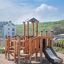 Rubik Modern Nature wooden playhouse with slide sur une aire de jeux sablonneuse