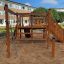 Cabane de jeu en bois avec toboggan, échelle d’escalade et bac à sable.