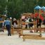 Des enfants et des adultes jouent sur l’équipement de jeu Balance à l’extérieur.