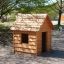 Structure en bois Nature Playhouse dans une aire de jeux entourée d'arbres.