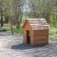 Structure en bois Nature Playhouse dans un parc avec une balançoire en arrière-plan.