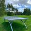 Outdoor Table Tennis dans un cadre extérieur herbeux avec des arbres en arrière-plan.