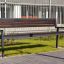 Oxford Bench, banc de parc moderne en bois foncé avec structure en métal dans un cadre urbain.