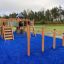 Structure de jeu en bois Somersault Triple sur une surface de sécurité bleue dans un environnement extérieur.