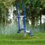 Équipement extérieur Cross Trainer dans un parc verdoyant entouré d’arbres et d’herbe.