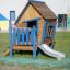 Maison de jeu en bois pour enfants Olle's Playhouse avec une échelle bleue et un toboggan.