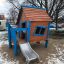 Maison de jeu en bois Olle's Playhouse avec des accents bleus et un toboggan dans un parc enneigé.