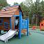 Maison de jeu en bois avec des accents bleus et un toboggan dans une aire de jeux intitulée Olle's Playhouse.