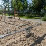 Double Seesaw en métal avec poignées rondes et ressorts, installé sur une aire de jeux sablonneuse.