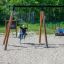 Des enfants jouent sur l’ensemble de balançoires Blackboard 156 cm dans une aire de jeux sablonneuse.