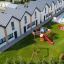 Tapis de sécurité en caoutchouc dans une aire de jeux pour enfants, à côté de maisons en rangée modernes et d’une piscine.