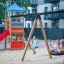 Enfants jouant sur la balançoire Nid d’oiseau avec tour (BNS 120 cm) avec un toboggan simple dans une aire de jeux.