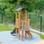Pixie Modern Nature wooden playhouse with slide sur l’aire de jeux avec échelle d’escalade et filet de sécurité