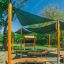 Salle de classe en plein air avec bancs en bois, pare-soleil et tableau noir dans un parc.