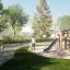 Des enfants jouent sur l’ensemble de jeu Alstad Eco dans un parc avec des arbres verts et de l’herbe.