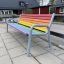 Colourful bench avec des lattes en bois arc-en-ciel et un cadre en métal gris sur une aire de jeux.