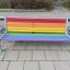 Colourful bench avec des lattes en bois aux couleurs de l'arc-en-ciel et un cadre en métal sur une zone extérieure pavée.