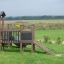 Fortress Nature playhouse with slide sur un champ herbeux avec des enfants qui jouent