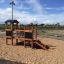 Fortress Nature playhouse with slide dans une aire de jeux sablonneuse