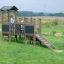 Fortress Nature playhouse with slide dans un champ vert avec un enfant qui joue.